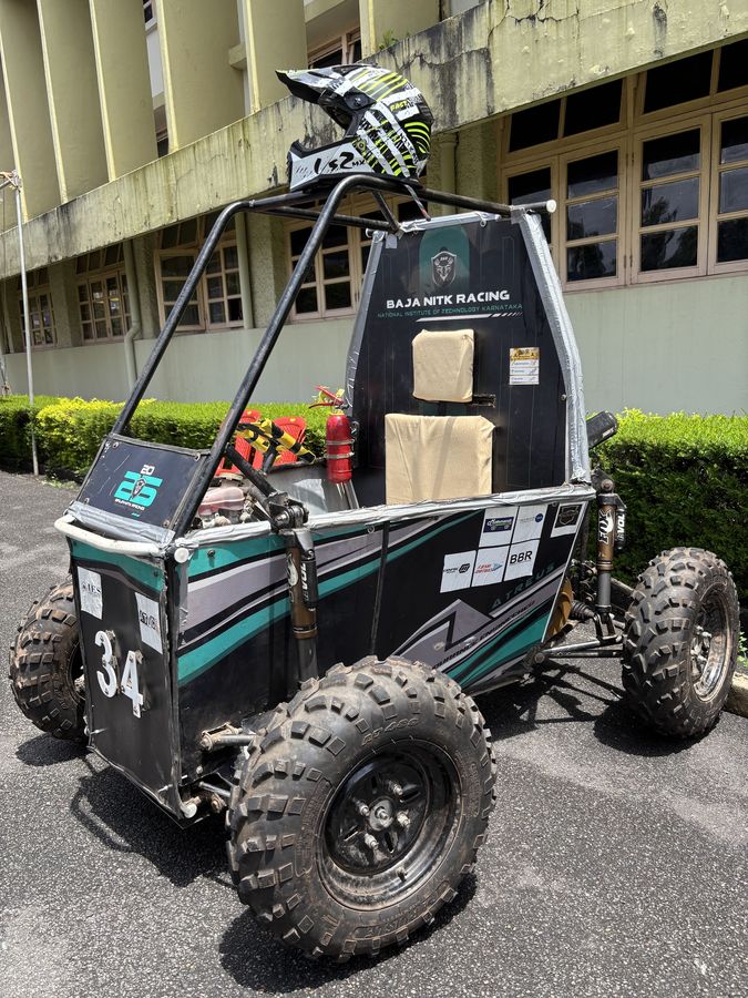 Front three-quarter view of the car on tarmac outside a campus building, a helmet resting on the roll cage
