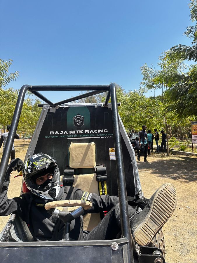 A helmeted driver strapped into the BNR car’s cockpit under a clear sky