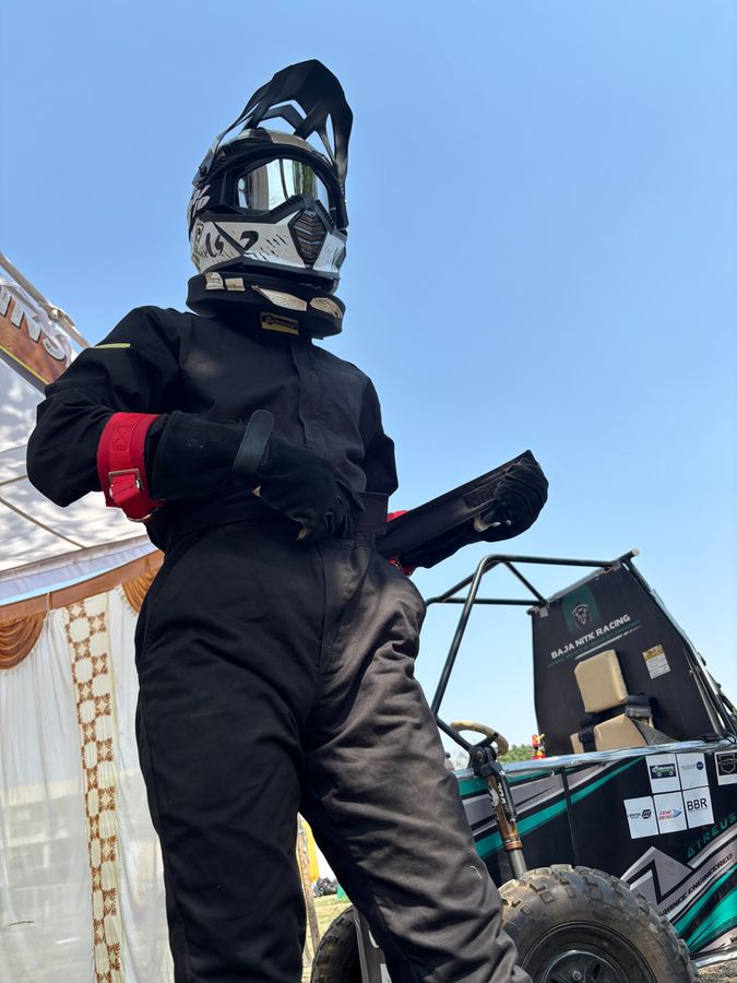 The driver in a black race suit and helmet standing beside the car