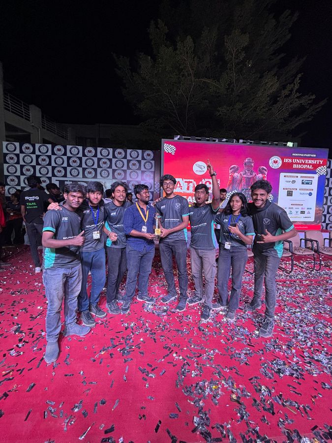 Team members in BNR jerseys on a confetti-covered stage holding a trophy