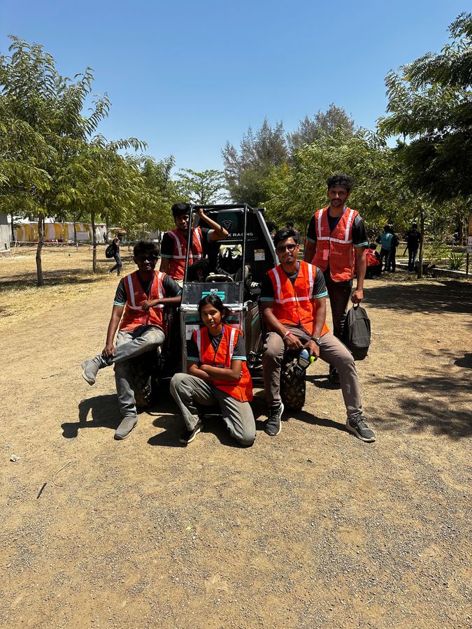 Team members in orange safety vests crouched around the car at the event grounds