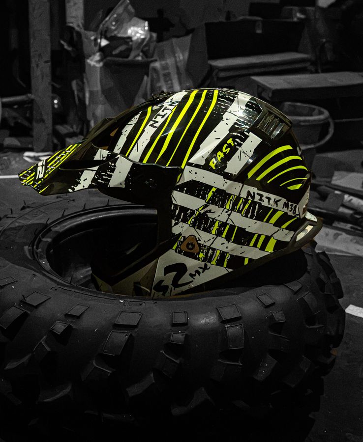 A black, white and neon-yellow racing helmet resting on an off-road tyre