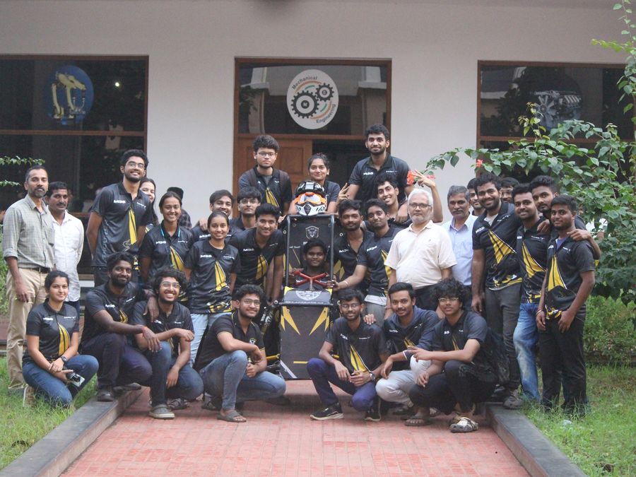 A large team photo with faculty in front of a campus building