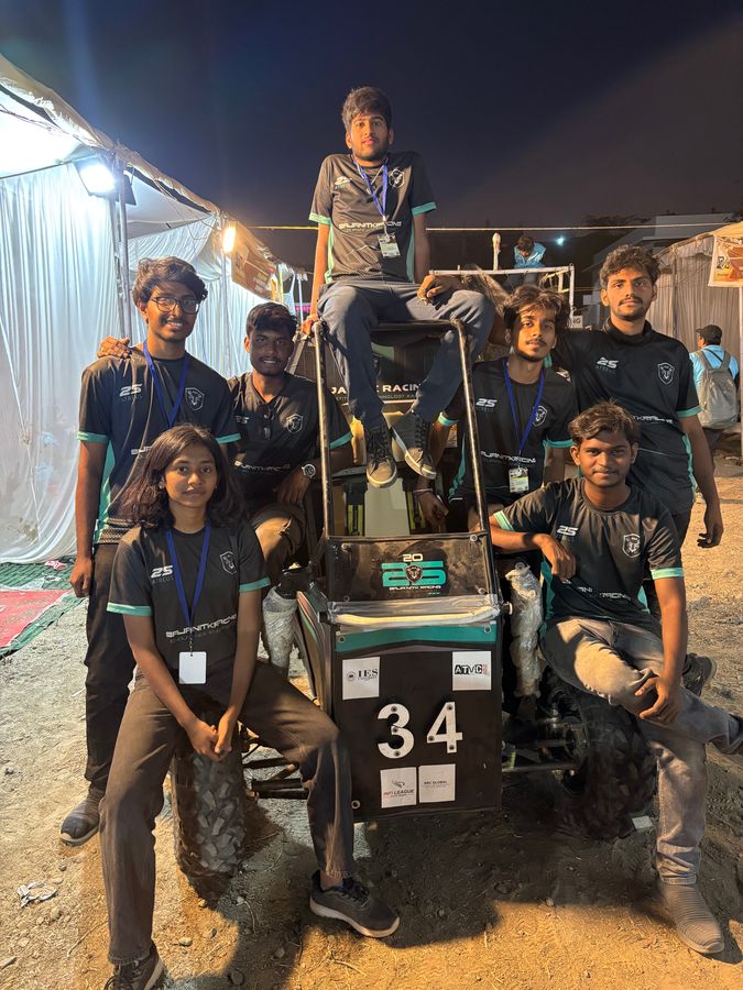 Team members in lanyards posing around car number 34 at night at the event
