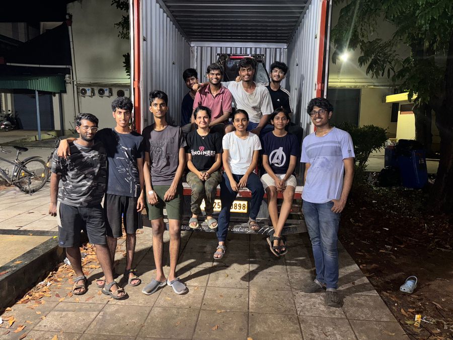 Team members sitting and standing together outside a workshop container at night