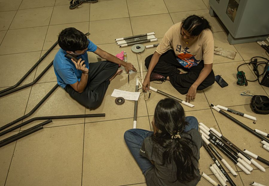 Overhead view of three team members on the floor measuring labelled roll cage tubes