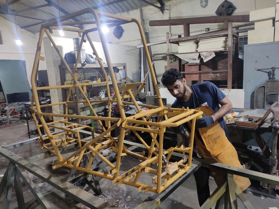 A team member fabricating the yellow tubular roll cage on a jig in the workshop