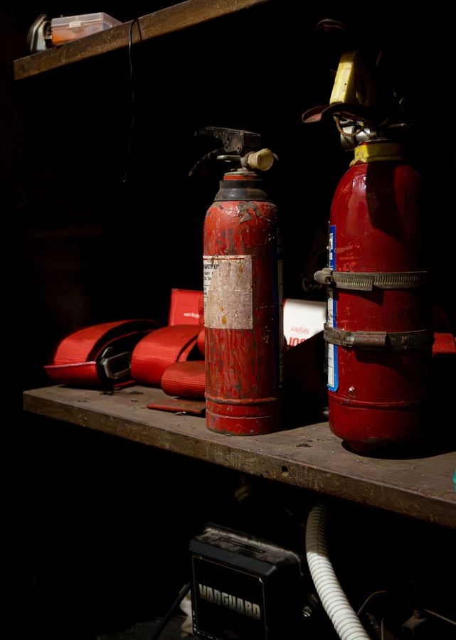 Two red fire extinguishers and red racing harness straps on a workshop shelf