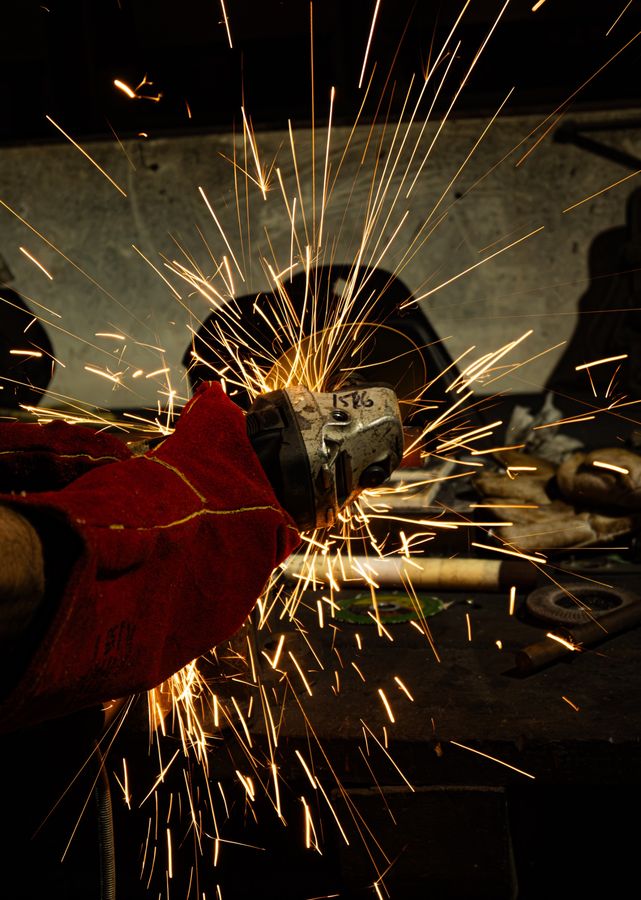 A gloved hand holding an angle grinder as sparks fan out in the dark