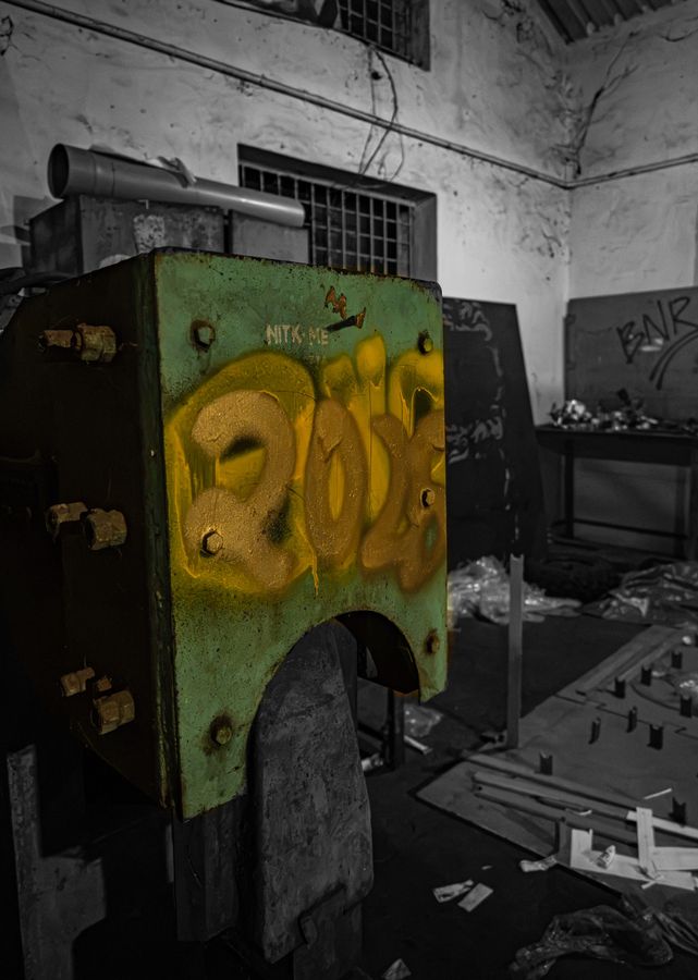 An old green workshop press sprayed with a yellow 2026, with BNR graffiti on the wall behind
