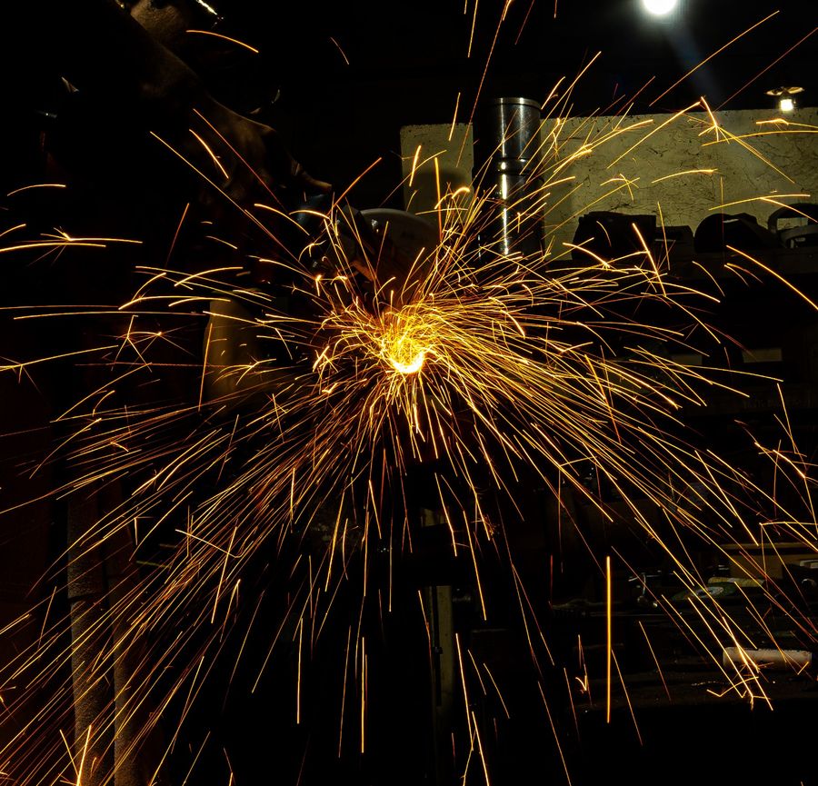 A dense burst of orange sparks from a grinder in a dark workshop